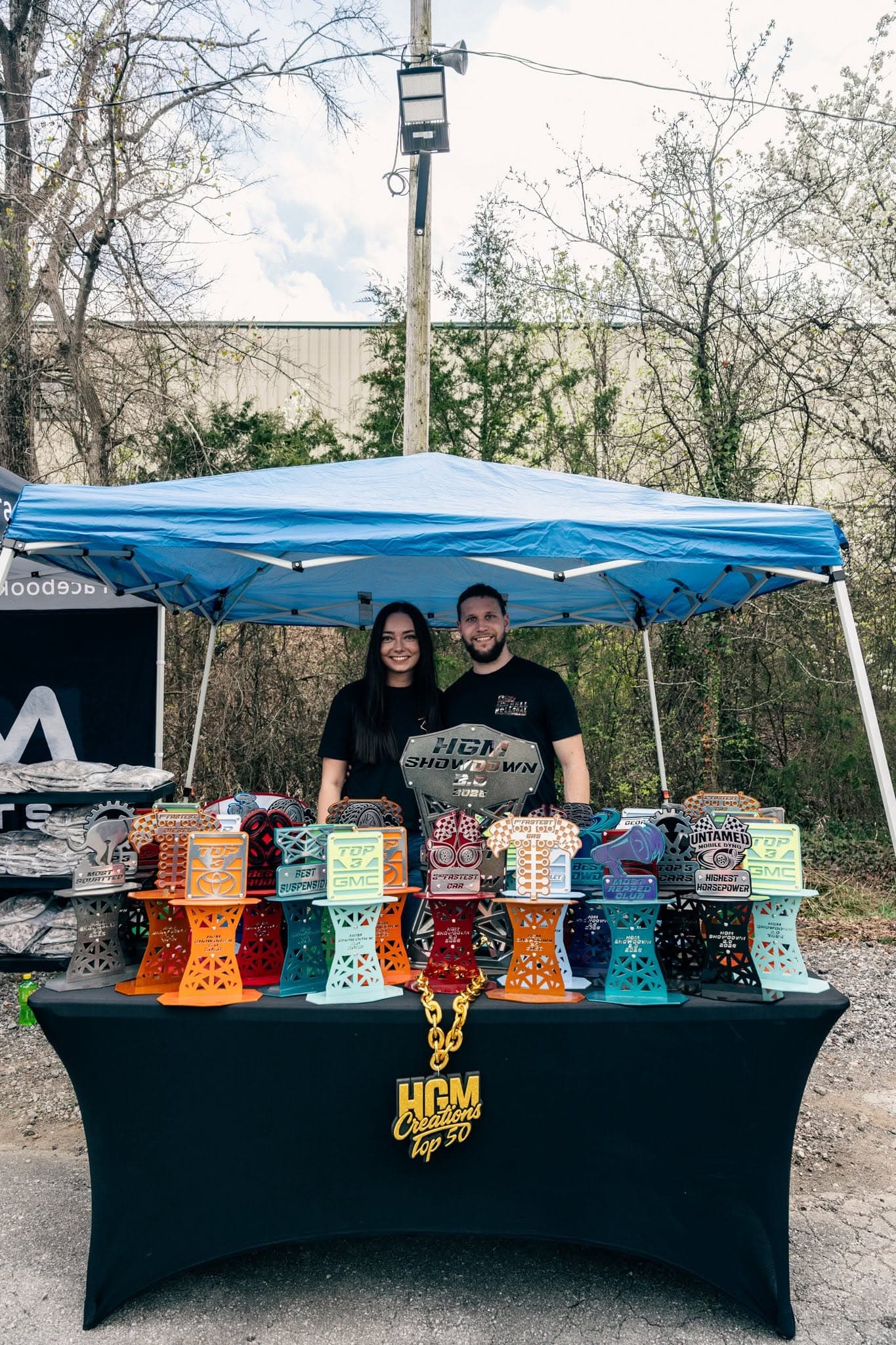 Matt Bond and his wife at a car show, behind a table of Bond Welding Service custom trophies